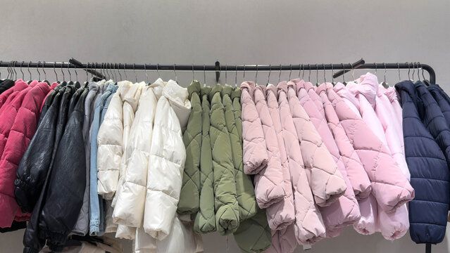 Neatly arranged winter jackets in soft pastel and neutral colors hang tightly on a clothing rack inside a modern retail store, creating an organized and stylish seasonal display