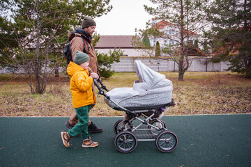 A father, son, and dog are walking in the park in autumn with a newborn in a stroller. A father walks with his children.