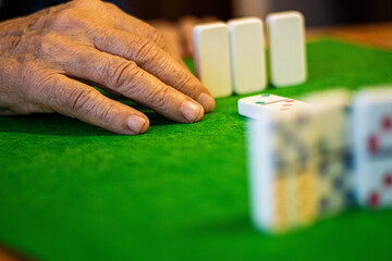 Senior Hand Playing Dominoes on Green Table