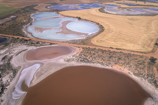 Aerial view of shimmering, pastel-colored salt lakes contrasting with the arid, ochre-toned earth, a starkly beautiful landscape, West Ballidu, Western Australia, Australia.