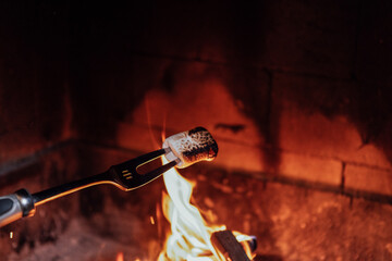 Marshmallow on a roasting fork is being toasted over a vibrant campfire, with glowing flames and warm embers creating a cozy outdoor atmosphere for gathering