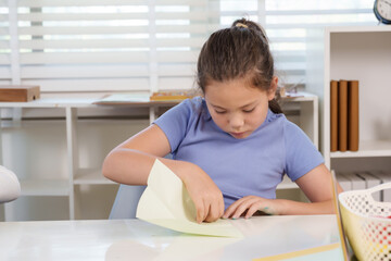 Naklejka premium Caucasian preteen girl leans forward folding large paper attentively during classroom origami project improving concentration teamwork creativity and motor skill engaging childhood education workshop