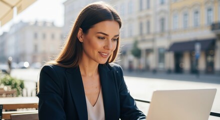 Smiling business woman working on a laptop at an outdoor cafe. Young professional female sitting in a city street setting. Remote work and digital nomad concept