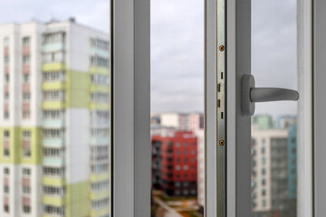 The handle and locking mechanism of an open plastic window against a background of blurred city high-risesThe handle and locking mechanism of an open plastic window against a background of blurred cit