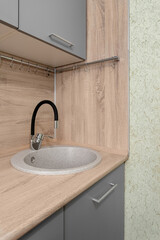 A fragment of a modern kitchen set with a sink and a flexible black faucet