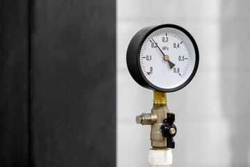 A round pressure gauge in a black case, installed on a pipeline with a valve, shows the pressure