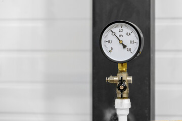 A round pressure gauge in a black case, installed on a pipeline with a valve, shows the pressure