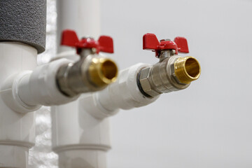 Two ball valves with red handles are installed on the plastic pipes of the water supply system