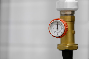 A round thermometer in a red case is installed on a brass fitting of the heating system
