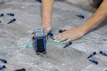 A craftsman's hands align the tile on the floor along the green line of a laser level
