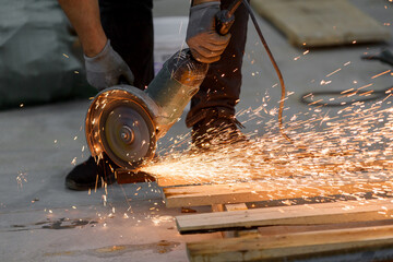 An angle grinder in a worker's hands cuts metal, scattering bright sparks