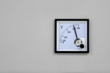 An analog voltmeter with a black pointer, mounted on a gray panel, shows a voltage above 400 volts