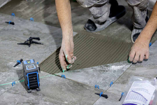 The process of laying floor tiles on an adhesive solution using a laser level and a leveling system