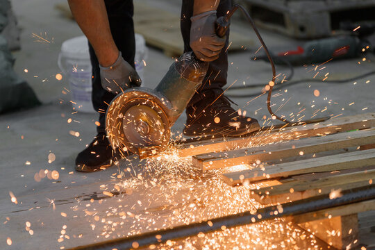 An angle grinder in a worker's hands cuts metal, scattering bright sparks