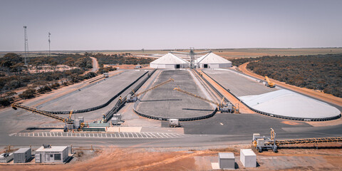 Aerial view of grain storage facilities bathed in the warm light, contrasting the industrial structures with the surrounding arid landscape, Ballidu, Western Australia, Australia.