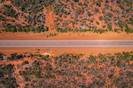 Aerial view of a long, straight road slicing through the red earth and sparse green vegetation, a stark contrast of colors and textures, Bullabulling, Western Australia, Australia.