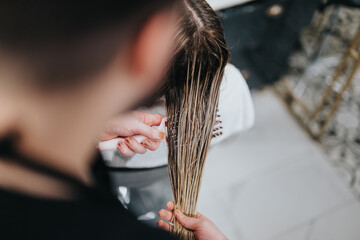 A stylist focuses on precision while cutting a long blonde client's hair in a clean, modern salon setting. The scene conveys professional grooming and beauty care in a calm environment.