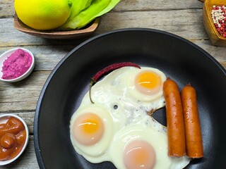 delicious appetizing breakfast of fried eggs and sausages on a frying pan