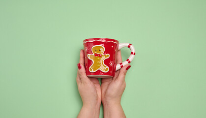 Two female hands holding a red Christmas mug with a gingerbread man on a green background.