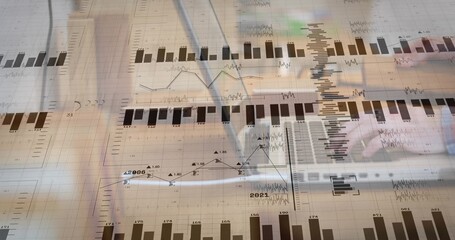 Analyzing hands wearing light-sleeved writing on paper at office desk, with pen, laptop and charts