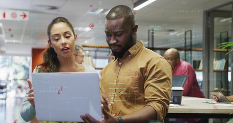 Reviewing two coworkers pointing at silver laptop in communal office, wearing business clothes