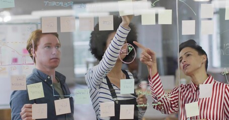 Collaborating team in blue shirt and red-blouse placing sticky notes on glass in office with marker