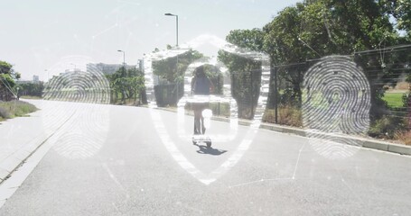 Riding adult woman wearing shorts and backpack skateboarding down paved road, with security overlay