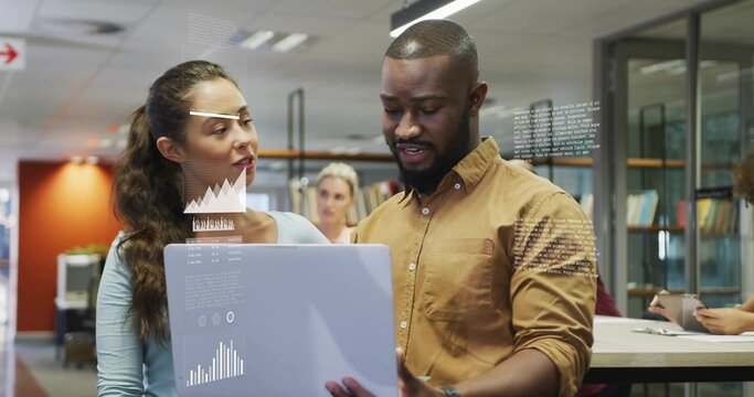Holding laptop, man in brown shirt explaining analytics, woman in blue top watching in open office - Powered by Adobe