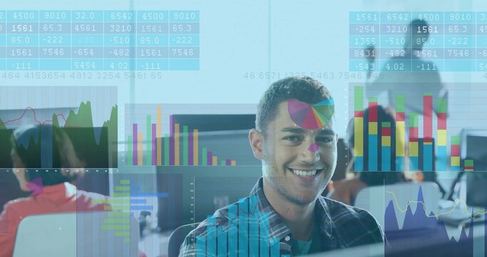 Smiling man in plaid shirt sitting at open-plan office desk, viewing translucent charts on monitors