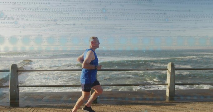 Jogging senior man in blue sleeveless top and black shorts along seafront path with railing, watch - Powered by Adobe