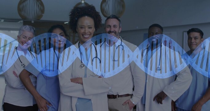 Posing center doctor crossing arms with staff in clinic, stethoscopes, coats, scrubs, DNA overlay - Powered by Adobe