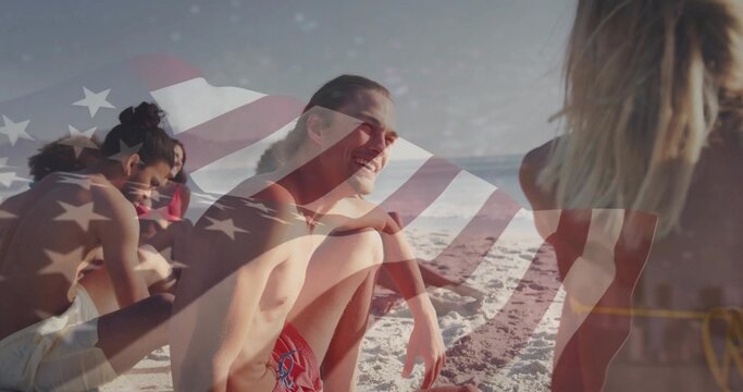 Smiling man wearing red swim trunks sitting at beach facing friends, with American flag overlay - Powered by Adobe