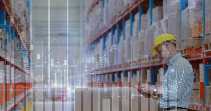 Warehouse worker wearing yellow hat operating tablet on boxes in aisle, racks, charts, copy space - Powered by Adobe
