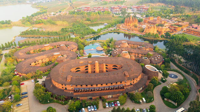 Aerial view of uniquely shaped buildings with brown rooftops nestled beside serene lakes, amidst verdant trees and clear skies, Honghe Hani and Yi Autonomous Prefecture, Yunnan, China.