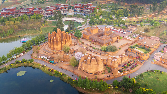 Aerial view of the striking architectural complex with its terracotta hues contrasting against the serene lake and lush landscape, Honghe Hani and Yi Autonomous Prefecture, Yunnan, China.