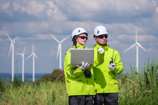 Engineers assess wind turbine performance while monitoring data at a renewable energy site in bright daylight