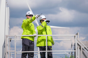 Technicians inspect wind turbines at a renewable energy facility during a cloudy afternoon