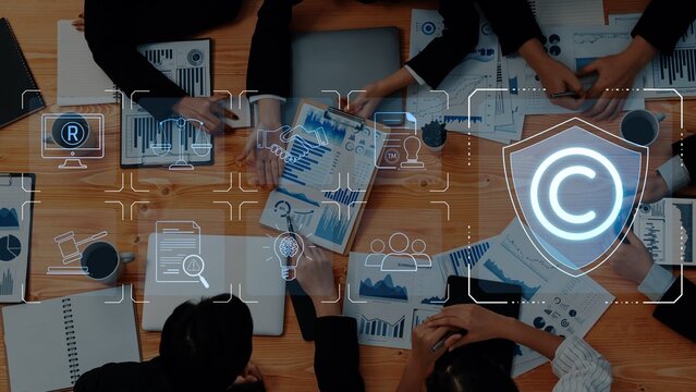 A high-angle view of business professionals discussing charts and documents while digital copyright symbols appear, showcasing teamwork and strategic planning in a modern workspace. Raster - Powered by Adobe