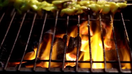 Close-up of juicy squid skewers sizzling on a hot BBQ grill. Oil drips onto the flames, creating dramatic fire and smoke. Intense street food scene for food vlogs, cooking, and culinary travel content