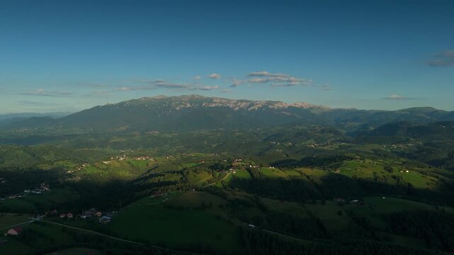 Aerial footage from Transylvania, Romania, golden hour drone flight over Pestera and Bran Rucar hills towards Bucegi Mountains ridge at sunset, panoramic landscape for eco tourism, rural travel