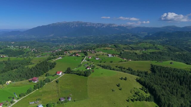 Drone flies over the rolling green hills of the Bran Rucar corridor with Bucegi Mountains ridge under a clear summer sky, aerial footage in Transylvania, Romania, eco tourism, countryside travel