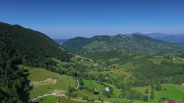 Panoramic view over rolling green hills with Bucegi Mountains ridge under a clear summer sky, aerial footage in Magura, Pestera villages, Transylvania, Romania, eco tourism, countryside travel