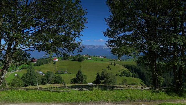 Spectacular reveal of the Bran Rucar corridor in Transylvania, Romania, aerial footage framed view of Pestera village houses scattered on green hills with western Bucegi ridge on a clear summer day