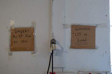 Two Hand-Written Cardboard Signs on a White Wall in a Laundromat, Stating Prices for Washers and Dryers