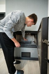 Young man carefully cleaning the inside of a sleek fireplace in a modern living room, focusing on removing ash and debris for a tidy appearance