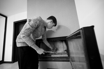 Man engaged in cleaning a fireplace in a cozy living room setting during a tranquil morning, showcasing dedication to home upkeep and personal space enhancement