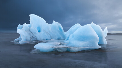 Aerial view of a luminous blue iceberg, sculpted by time and tide, rests serenely on the glacial sands of Jokulsarlon lagoon, Sveitarfelagid Hornafjordur, Iceland.