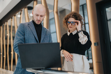 Two professionals analyze a laptop in a contemporary office lobby, signaling teamwork, planning, and business collaboration in a stylish, urban setting.