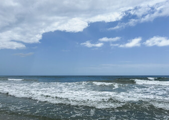 Ocean Waves Crashing on Shore Under Blue Sky with White Clouds