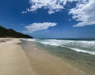  Panoramic view of Cuyagua, Venezuela, a tropical beach with golden sand, rolling waves, and a lush green hill in the background
